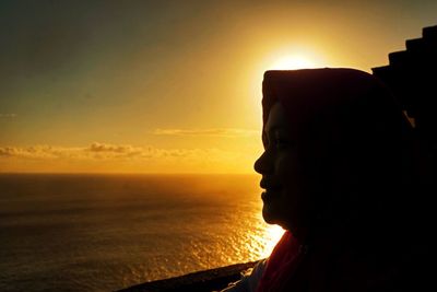 Side view of smiling woman standing by sea against sky during sunset