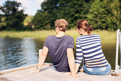Rear view of mature couple relaxing on pier at lake
