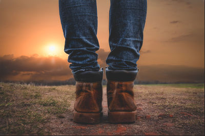 Low section of man wearing jeans standing on grass during sunset