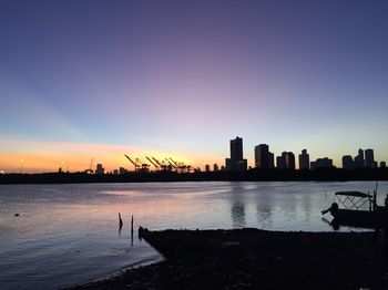 Silhouette buildings by sea against sky during sunset