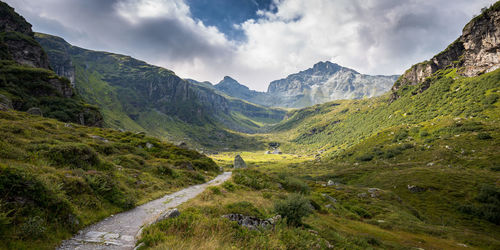 Footpath on green landscape with mountains against sky