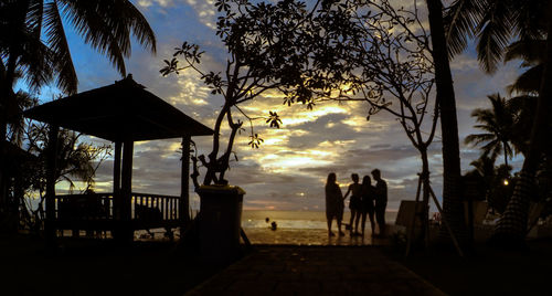 Silhouette people on sidewalk against sky during sunset