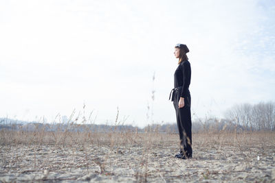 Side view of young woman standing on field against sky