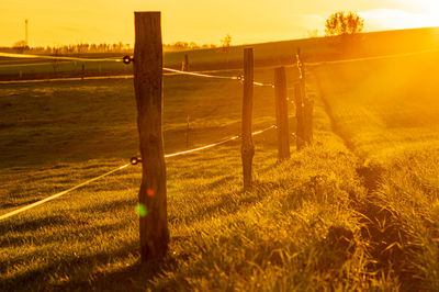 Wooden fence on field against sky during sunset
