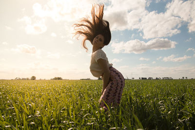 Side view of young woman tossing hair while standing on agricultural field