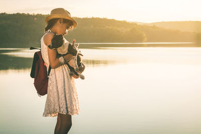Portrait of woman standing by lake against sky during sunset
