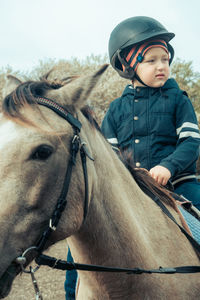 Cute boy sitting on horse against sky