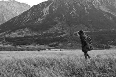 Person walking on grassy field against mountains