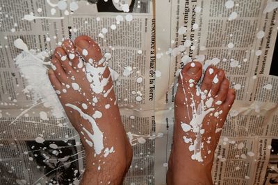 Cropped image of legs with white paint standing on newspaper