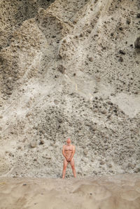 High angle view of shirtless adult man standing on beach against rock