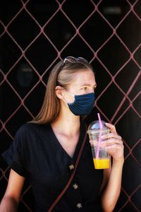 Young woman drinking water against fence