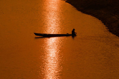 Silhouette man in sea against sky during sunset