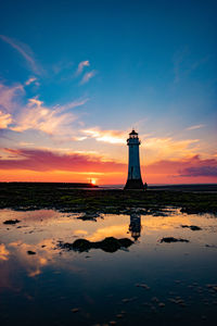 Lighthouse by sea against sky during sunset