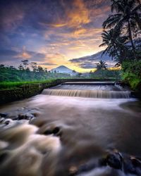 Scenic view of lake against cloudy sky during sunset