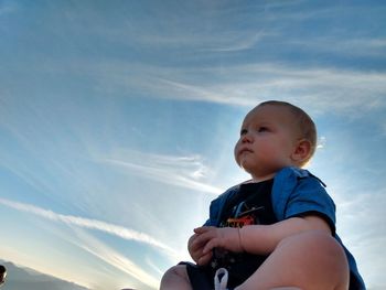 Low angle view of cute baby boy looking away against sky