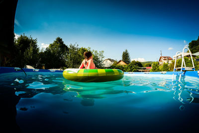 Girl with inflatable ring floating on wading pool at tourist resort against blue sky