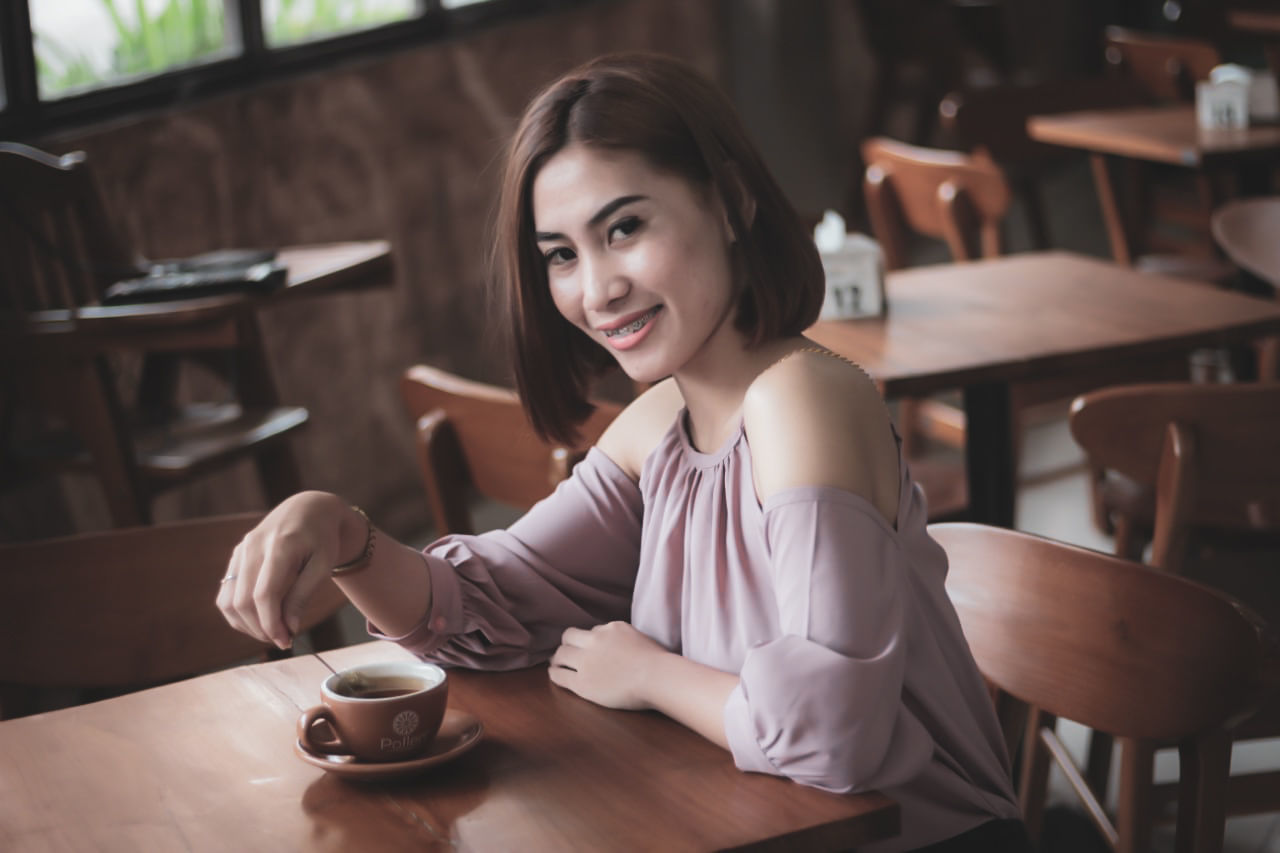 PORTRAIT OF YOUNG WOMAN SITTING AT TABLE WITH COFFEE