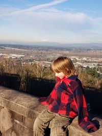 Rear view of boy sitting on landscape against sky