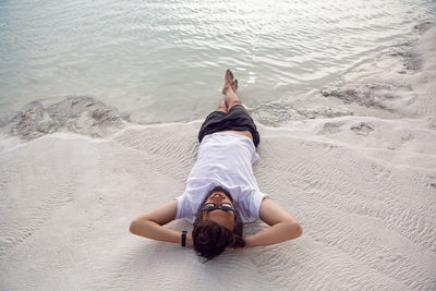 Man with a beard in a white t-shirt and shorts rest on a white mountain in pamukkale