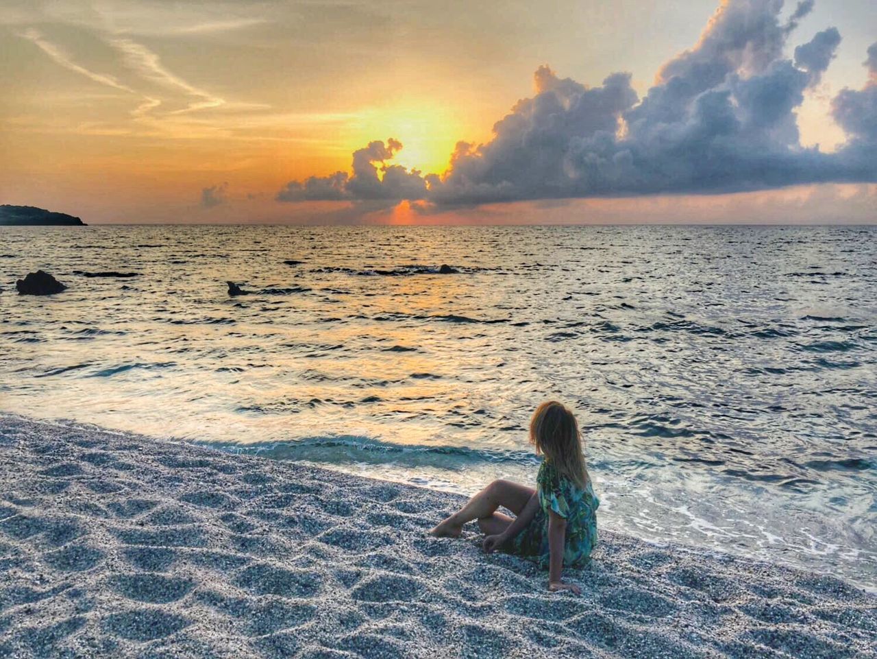 WOMAN SITTING ON SHORE AT SUNSET