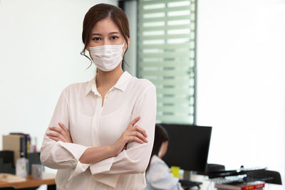 Portrait of businesswoman wearing mask gesturing while standing in office
