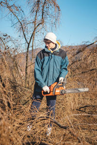 Young 17-year-old temporary worker in work clothes wrestles with a chainsaw and a dry larch tree