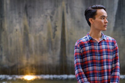 Young man looking away against wall