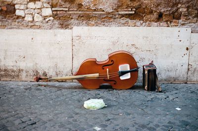View of violin placed on street against weathered wall