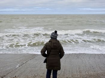 Rear view of woman standing on beach against sky