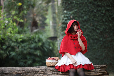 Woman looking away while sitting on wood against trees