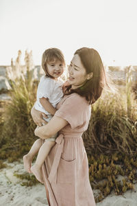 Mid view of mother holding young girl at beach during sunset