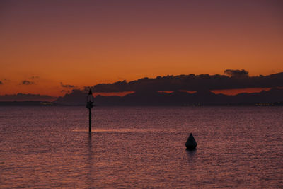 Silhouette sailboat in sea against orange sky