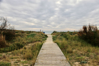 Boardwalk leading towards landscape against sky