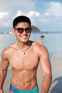 Portrait of shirtless young man wearing sunglasses against sea