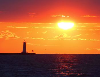 Silhouette lighthouse at sea against sky during sunset