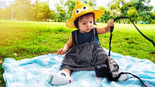 Baby girl playing with camera while sitting in park