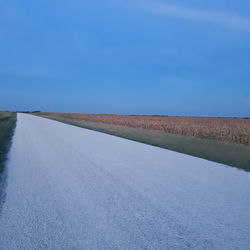 Country road amidst field against blue sky