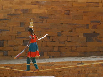 Side view of a girl walking on rope against brick wall