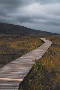 Boardwalk leading towards mountains against sky
