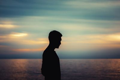 Silhouette man standing by sea against sky during sunset