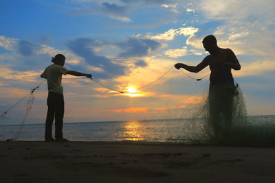 Fishermen holding fishing net on beach at sunset