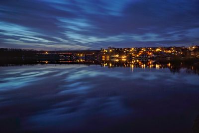 Illuminated city by sea against sky at night