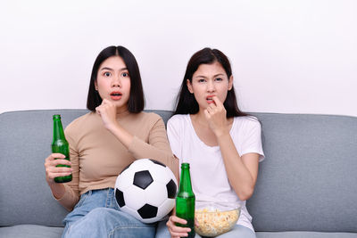 Portrait of shocked young friends watching soccer match on sofa at home