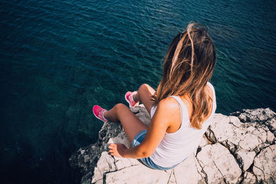 Rear view of woman sitting on rock by sea