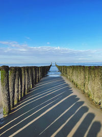 Empty road leading to sea against blue sky