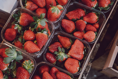 Top view of fresh strawberries on sale, portioned in plastic boxes, on top of a wooden table.