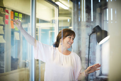 Smiling businesswoman discussing while pointing at sticky notes in creative office