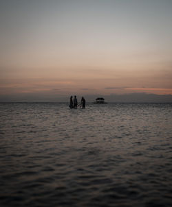 Silhouette people on sea against sky during sunset