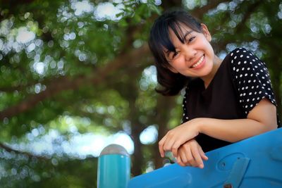 Portrait of smiling young woman against trees at playground