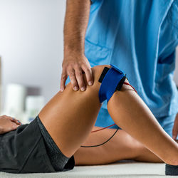 Midsection of physical therapist using electrical stimulation on womans knee for treatment
